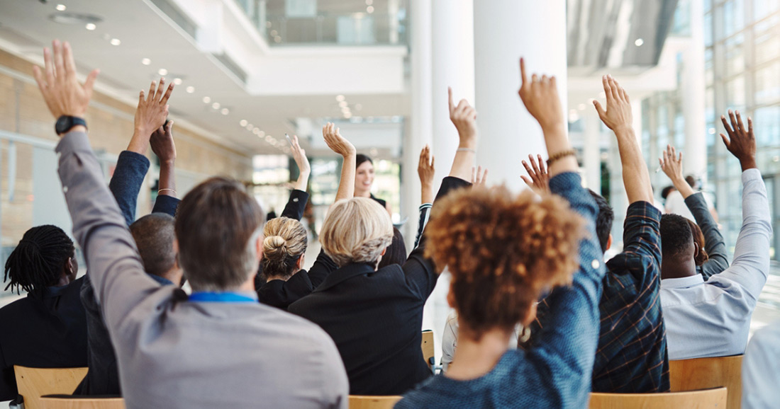 Group of people raising their hands to ask questions during a meeting.