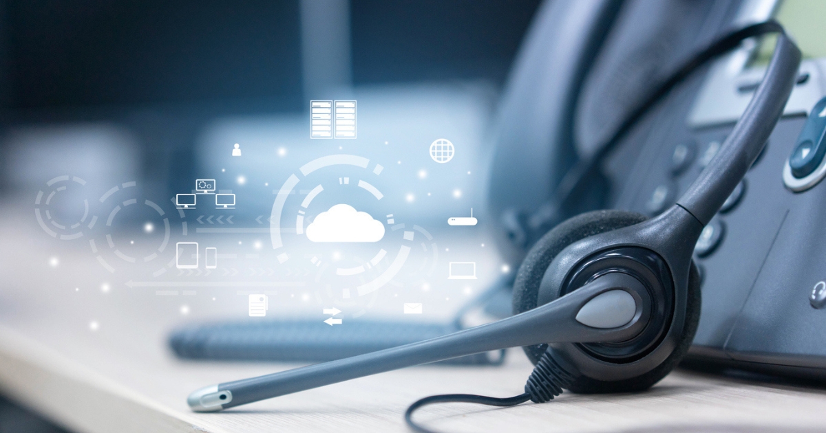 Call center headset resting on a desk, next to a modern office phone. Overlaying the image are digital icons representing cloud computing, data storage, and communication technology, symbolizing the integration of cloud-based systems in call centers.