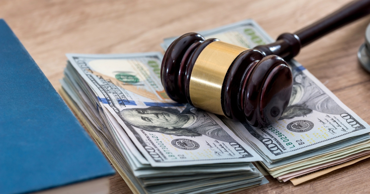 Gavel rested on a stack of hundred-dollar bills next to a blue folder, symbolizing legal and financial consequences.