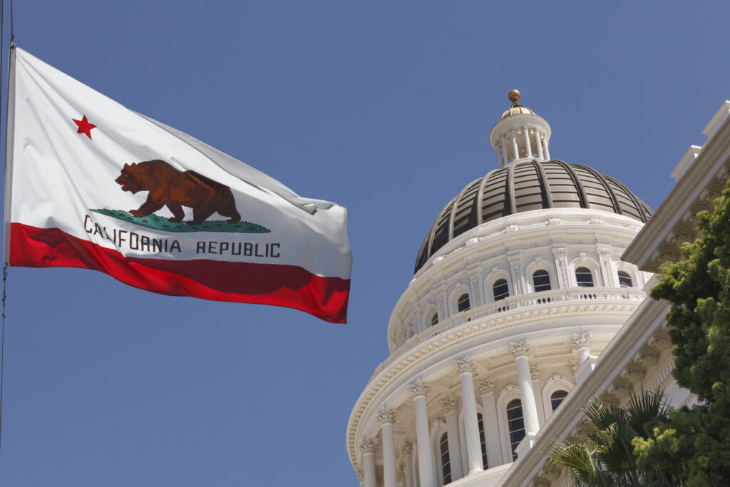 California state flag waving in the wind next to the California State Capitol building.