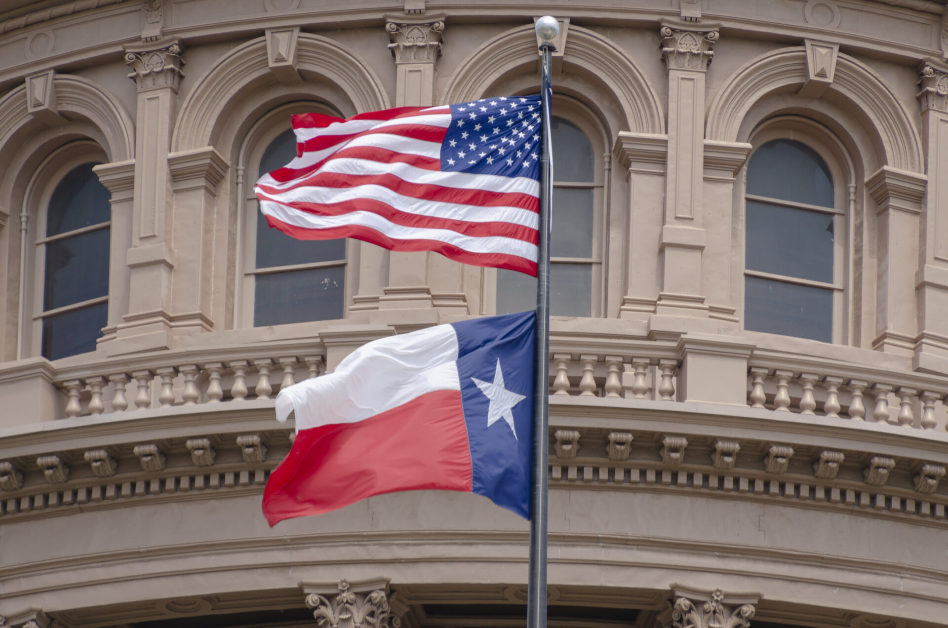 The United States and Texas State flags flying in front of the Texas Capitol building in Austin