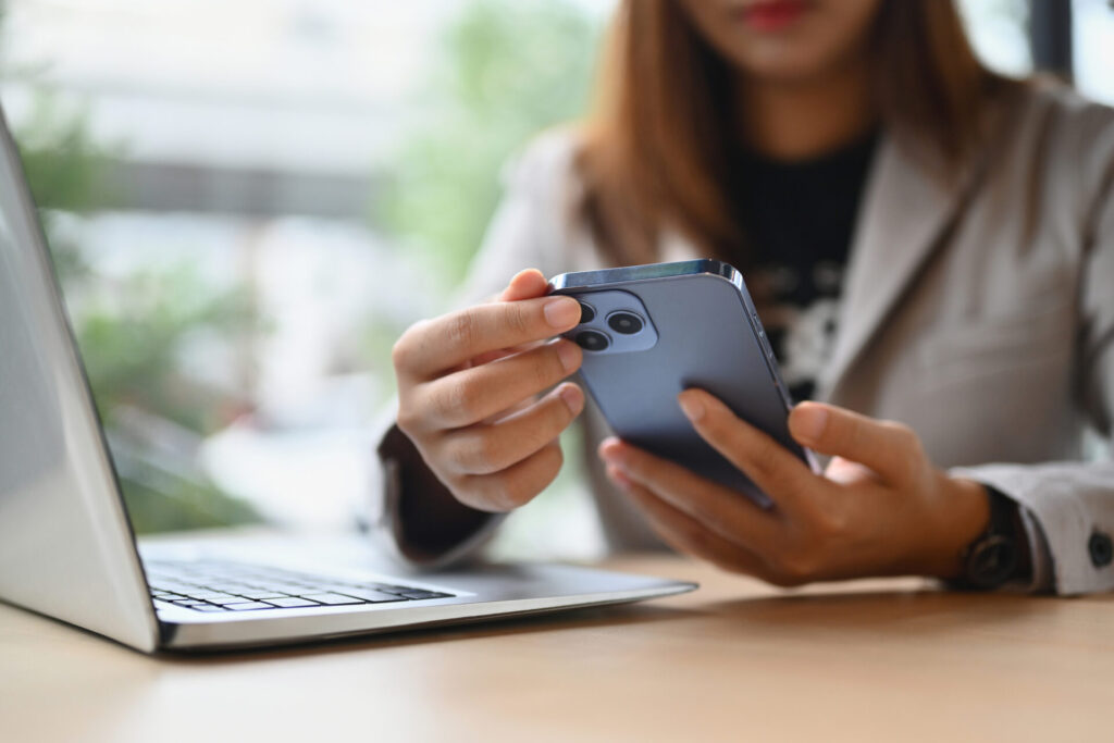 Women looking at her iPhone and reviewing an incoming phone call. She is sitting at a desk with a laptop next to her.