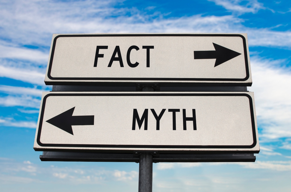 Two road signs pointing in different directions: one points right towards “fact,” the other points left towards “myth.”