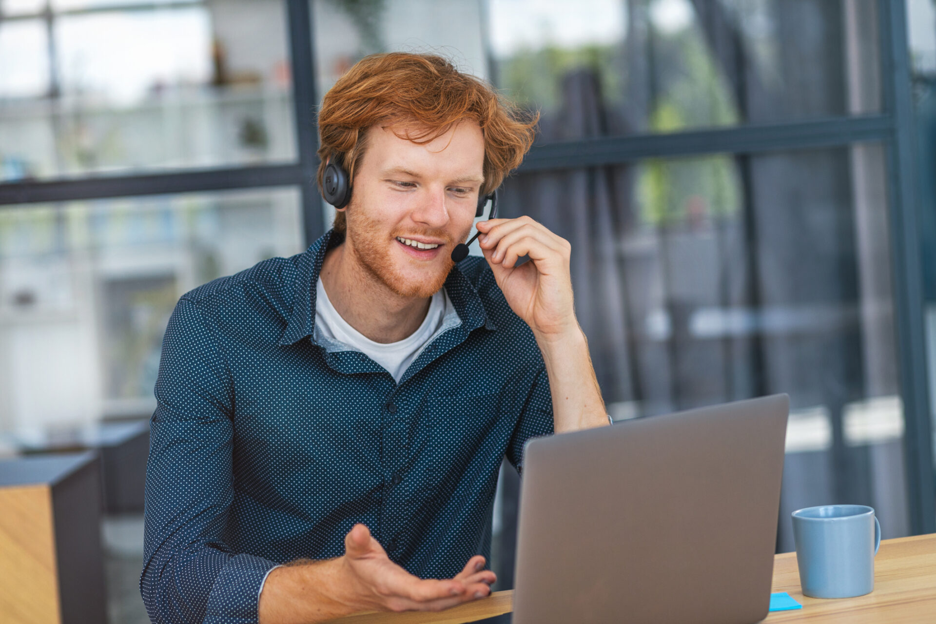 Man wearing a headset and smiling while on a sales call. He is seated at a desk with a laptop to represent him using a single line dialer to make the call.