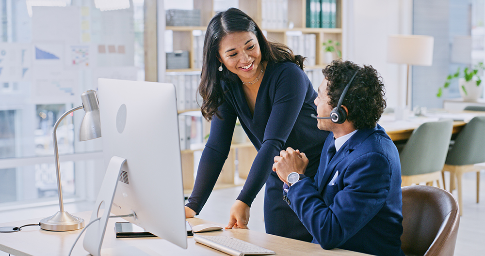 Sales manager talking to an agent wearing a headset at their desk, illustrating training on outbound call compliance and best practices.